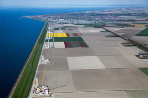 A dike, the green strip along the coast, protects flower fields and wind turbines in the northern Netherlands.
