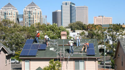 Workers put solar panels on a house near downtown Oakland under a program that uses revenue from California’s cap-and-trade auctions.
  