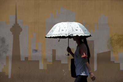 A woman shields herself from the sun as she passes a mural in Beijing in July 2015.