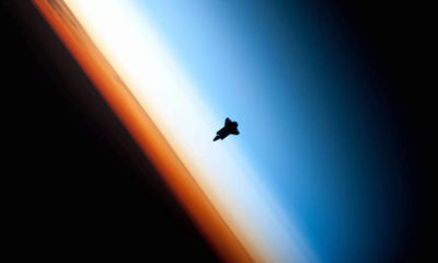 A view of the space shuttle Endeavor showing several layers of the atmosphere — the mesosphere (blue), the stratosphere (white), and the troposphere (orange).