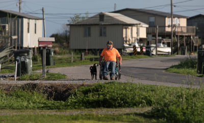 Chris Brunet and his dog Precious survey the empty camps and buildings near his home on Isle de Jean Charles in February 2018. Brunet said he feels like the grant money should have been just for the tribe. It's OK to help other people with the money, he said, but the tribe should be in one place, held together as one community. Alone.