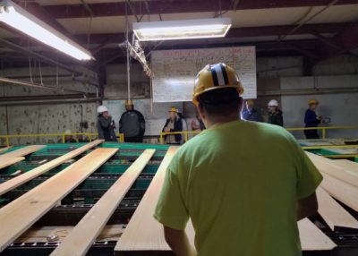 An inspector grades lumber at the Menominee sawmill, with visitors on tour in the background. 
